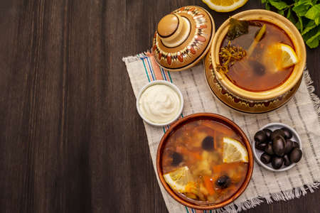 Hodgepodge, hot soup served in traditional ceramic bowl and pot. Classical Eastern Europe dish, trendy black wooden backgroundの写真素材