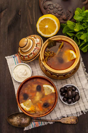Hodgepodge, hot soup served in traditional ceramic bowl and pot. Classical Eastern Europe dish, trendy black wooden backgroundの写真素材