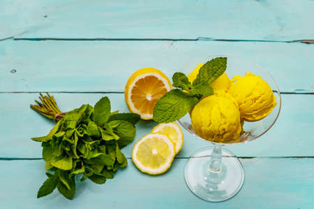 Lemon ice cream with mint. Refreshing summer dessert, ripe fruit, fragrant leaves. Trendy turquoise wooden background, close upの写真素材