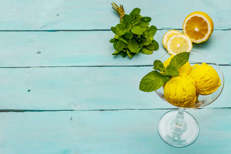 Lemon ice cream with mint. Refreshing summer dessert, ripe fruit, fragrant leaves. Trendy turquoise wooden background, copy spaceの写真素材
