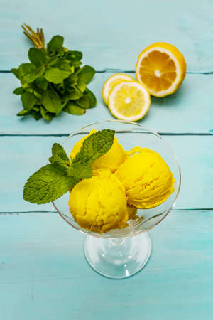 Lemon ice cream with mint. Refreshing summer dessert, ripe fruit, fragrant leaves. Trendy turquoise wooden background, top viewの写真素材