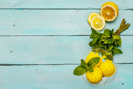 Lemon ice cream with mint. Refreshing summer dessert, ripe fruit, fragrant leaves. Trendy turquoise wooden background, top viewの写真素材