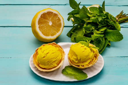 Lemon ice cream with mint. Refreshing summer dessert, ripe fruit, fragrant leaves. Trendy turquoise wooden background, close upの写真素材