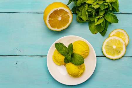 Lemon ice cream with mint. Refreshing summer dessert, ripe fruit, fragrant leaves. Trendy turquoise wooden background, top viewの写真素材