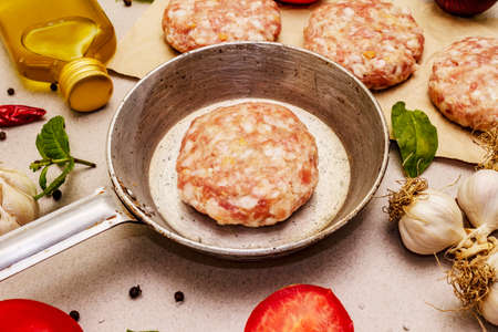 Raw cutlets, fresh vegetables, spices, olive oil. Vintage pan, picnic or barbecue cooking concept. Stone concrete background, close upの写真素材