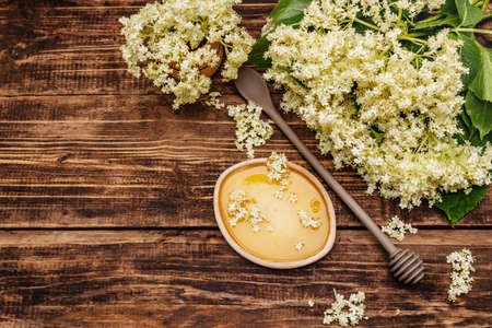 Honey and fresh elder flowers. Fragrant bouquet, alternative medicine. Old wooden boards background, top viewの写真素材