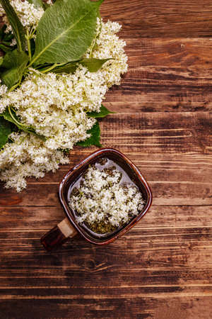 Tea from fresh elder flowers. Hot drink, alternative medicine. Old wooden boards background, top viewの写真素材