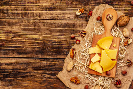 Pieces of aged Gouda cheese. Pecans, walnuts and hazelnuts. Cutting board, vintage wooden table, top viewの写真素材