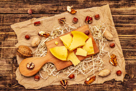 Pieces of aged Gouda cheese. Pecans, walnuts and hazelnuts. Cutting board, vintage wooden table, top viewの写真素材