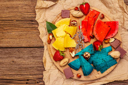 Cheese plate. Assorted multicolored hard Dutch cheeses. Blue and red pesto, aged gouda. Strawberry, chocolate, nuts, herbs and flower. Old wooden boards background, top viewの写真素材