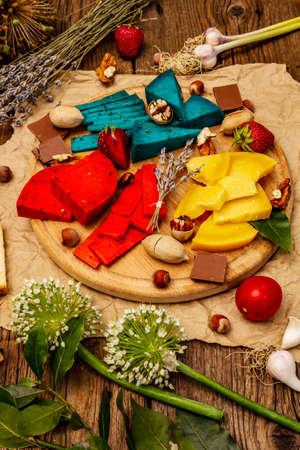 Cheese plate. Assorted multicolored hard Dutch cheeses. Blue and red pesto, aged gouda. Strawberry, chocolate, nuts, herbs and flower. Old wooden boards background, close upの写真素材