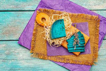 Dutch blue cheese with lavender. Piece and slices, dry fragrant flower, cutting board. Trendy turquoise wooden boards background, top viewの写真素材