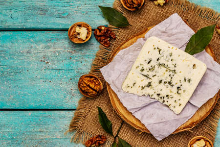 Cheese with blue mold. Ingredient for a cheese plate. Nuts, fragrant bay leaves, knife. Trendy turquoise wooden boards background, top viewの写真素材