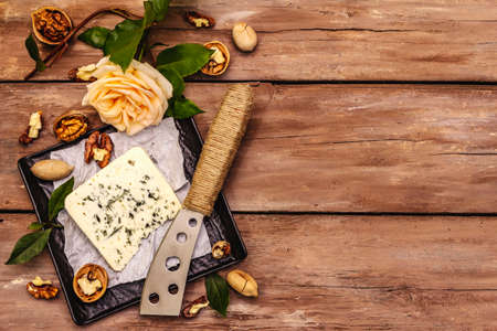 Cheese with blue mold. Ingredient for a cheese plate. Nuts, fragrant bay leaves, knife. Wooden...