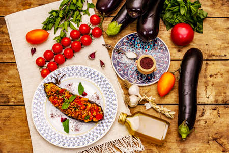 Karniyarik traditional Turkish food. Stuffed eggplants with minced meat, tomato, greens and sesame seeds. The dish was served on an old wooden table, top viewの写真素材