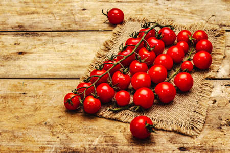 Whole ripe cherry tomatoes on branch. New harvest, on sackcloth, wooden boards background, copy spaceの写真素材