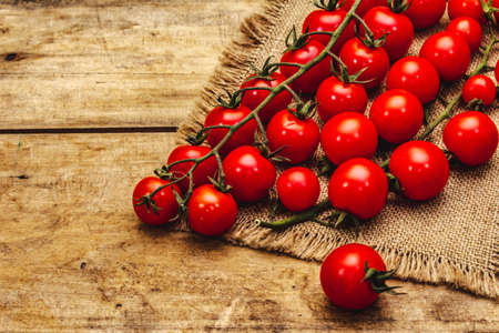 Whole ripe cherry tomatoes on branch. New harvest, on sackcloth, wooden boards background, copy spaceの写真素材