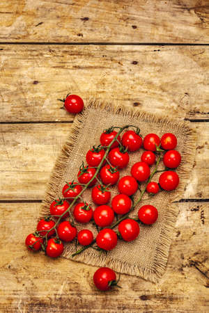 Whole ripe cherry tomatoes on branch. New harvest, on sackcloth, wooden boards background, top viewの写真素材