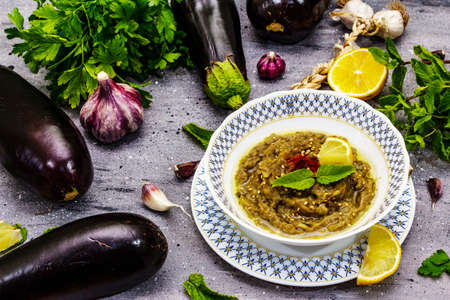 Eggplant dip baba ganoush (mutabbal) or mezze with ripe vegetables and fresh herbs. Traditional Middle East cuisine, healthy appetizer, vegan hummus. Stone concrete background, close upの写真素材