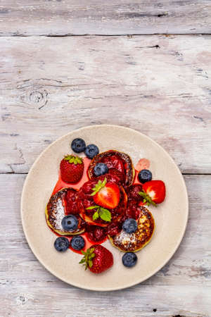 Cottage cheese pancakes with fresh berries and strawberry sauce. Healthy breakfast concept. Ripe blueberry, fragrant mint leaves. Wooden boards background, top viewの写真素材