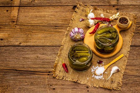 Marinated pickled cucumbers with spices and herbs. Traditional homemade fermented appetizer in glass jars. Vintage wooden boards background, top viewの写真素材