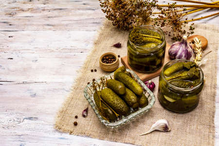 Marinated pickled cucumbers with spices and herbs. Traditional New Year appetizer in glass jars and crystal plate. White wooden boards background, copy spaceの写真素材