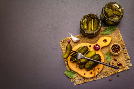 Marinated pickled cucumbers with spices and herbs. Traditional Eastern Europe appetizer in glass jars and on wooden cutting board. Trendy black stone concrete background, top viewの写真素材