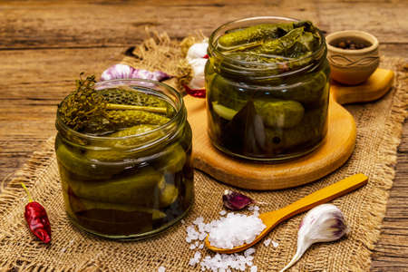 Marinated pickled cucumbers with spices and herbs. Traditional fermented appetizer in glass jar. Wooden boards background, top viewの写真素材