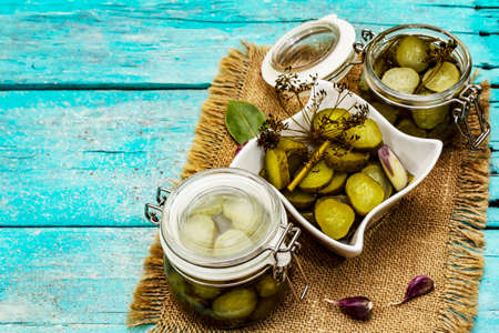 Marinated pickled cucumbers with spices and herbs. Traditional fermented appetizer in glass jar and ceramic bowl. Turquoise wooden boards background, copy spaceの写真素材
