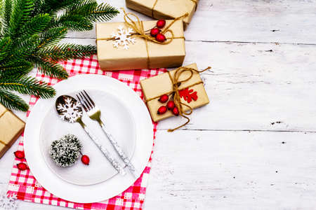 Christmas or New Year zero waste dinner place setting. Ceramic plates, gift, snowflakes, briar berries and thematic decor. Festive cutlery on white wooden boards background, top viewの写真素材