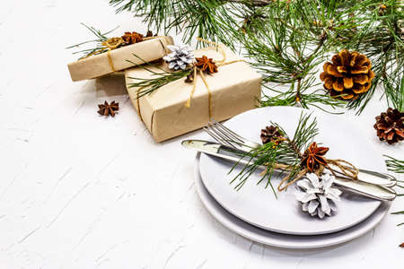 Christmas or New Year table setting. Festive cutlery, ceramic plates with fresh pine branch, cones, zero waste gifts and star anise. White putty background, copy spaceの写真素材