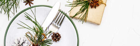 Christmas or New Year table setting. Festive cutlery, ceramic plates with fresh pine branch, cones, zero waste gifts and star anise. White putty background, banner formatの写真素材