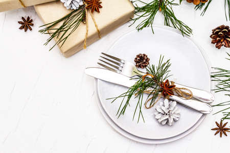 Christmas or New Year table setting. Festive cutlery, ceramic plates with fresh pine branch, cones, zero waste gifts and star anise. White putty background, top viewの写真素材
