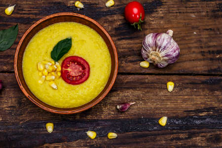 Corn cream soup with fresh vegetables, herbs and spices. Classic autumn hot dish, old wooden table, top viewの写真素材