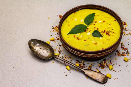 Corn cream soup with fresh vegetables, herbs and spices. Classic autumn hot dish, stone concrete background, copy spaceの写真素材