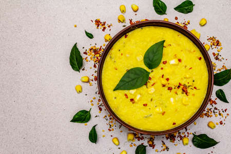 Corn cream soup with fresh vegetables, herbs and spices. Classic autumn hot dish, stone concrete background, top viewの写真素材