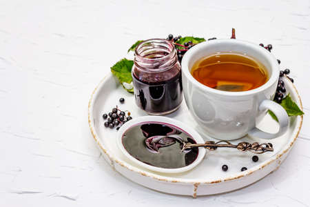Elderberry jam, syrup, confiture and hot tea. Ripe berries, sweet and healthy dessert. Alternative medicine and lifestyle. White putty background, copy spaceの写真素材
