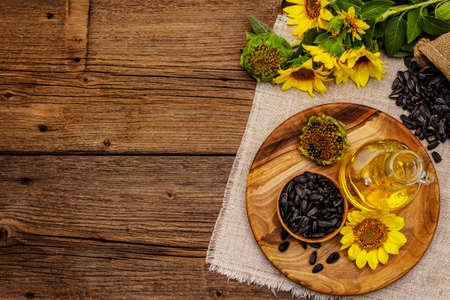Sunflower oil in glass cruet with flower head and seeds in wooden bowl. Vintage wooden boards background, rural still-life, top viewの写真素材