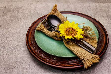Autumn and Thanksgiving dinner place setting. Sunflower bouquet, ceramic plates and sackcloth napkin. Fall black cutlery on stone concrete background, copy spaceの写真素材