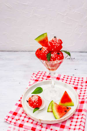 Sweet watermelon ice cream with coconut flakes and fresh basil leaves. Healthy dessert, white wooden boards background, close upの写真素材