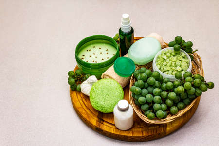 Natural spa accessories and green grapes placed on a wooden plate. Fresh ingredients for healthy and comfortable self care. Stone concrete background, copy spaceの写真素材