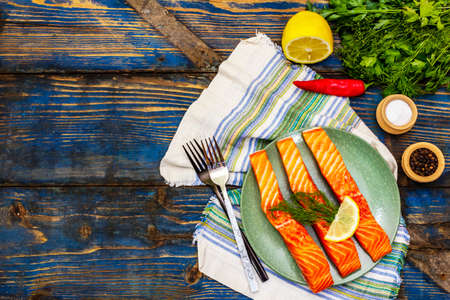 Raw Norwegian Trout. Pieces of fresh fish, cutlery, lemon, dill, pepper, greens, salt. Old wooden boards tableの写真素材