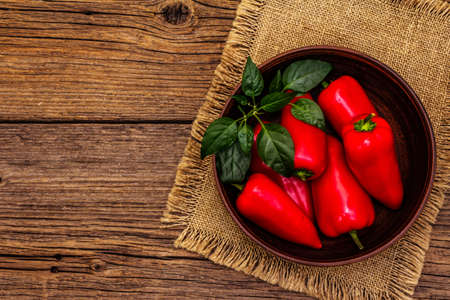 Ripe whole red mini peppers in clay bowl. Fresh harvest, traditional ingredient for cooking food. Vintage wooden boards table, top viewの写真素材