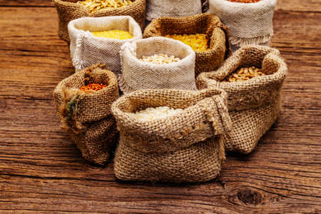 Assorted variety of cereals. An indispensable ingredient for a healthy diet. Handmade bags, old wooden boards background, top viewの写真素材