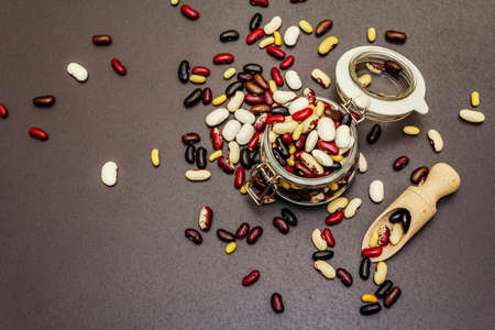 Assorted different types of beans in glass jar. Mix of various dry legumes on black stone concrete...