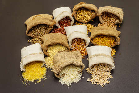 Assorted variety of cereals in handmade sacks. Mix of indispensable ingredients for a healthy diet. Black stone concrete background, close upの写真素材