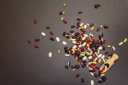 Assorted different types of beans in wooden scoop. Mix of various dry legumes scattered on black...