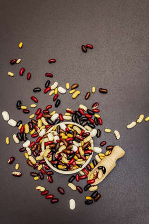 Assorted different types of beans in ceramic bowl. Mix of various dry legumes scattered on black stone concrete background, top viewの写真素材