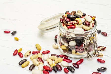 Assorted different types of beans in glass jar. Mix of various dry legumes on white putty...