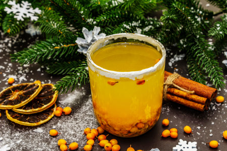 Festive low alcoholic fruit cocktail with fresh sea buckthorn berries, dry lemon slices and cinnamon sticks. Christmas or New Year sweet drink, evergreen fir branches. Black stone background, close upの写真素材